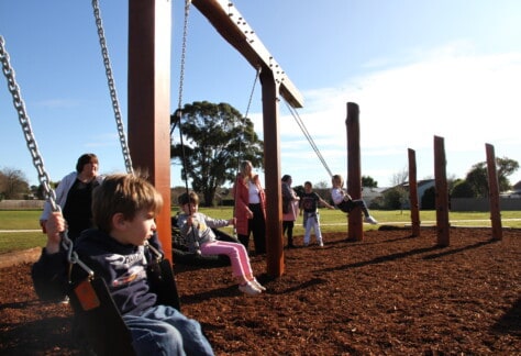 Children in swings at a playground that has a nature appearance