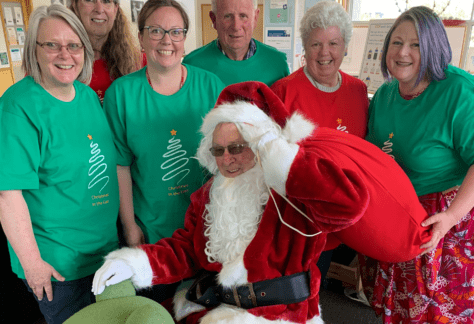 A group of people in Christmas t-shirts, standing around a man dressed as Santa to promote the annual Christmas in the East Santa Run.