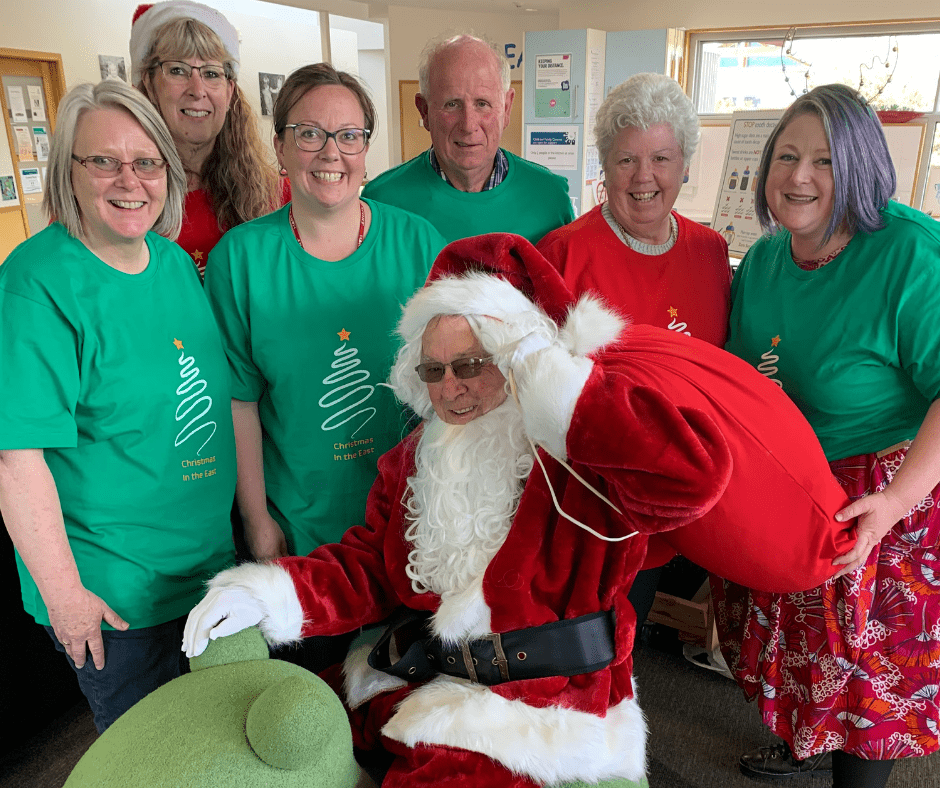 A group of people in Christmas t-shirts, standing around a man dressed as Santa to promote the annual Christmas in the East Santa Run.