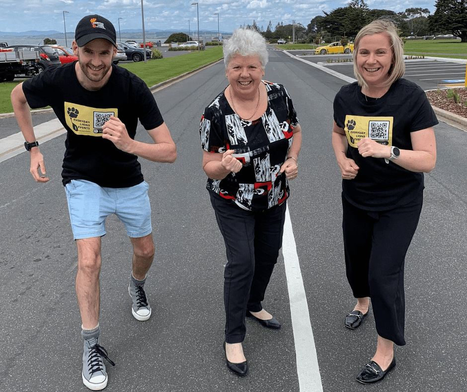 Three people pictured standing in a row pretending to be getting ready for a race, Run Devonport. The people are (from left) race director Brian Lyons, Devonport Mayor Annette Rockliff and fellow race director Amie Bramich, standing on the road near the Bluff.