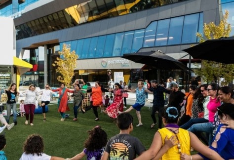 A group of people in a circle dancing to celebrate Harmony Day - outside the paranaple centre.