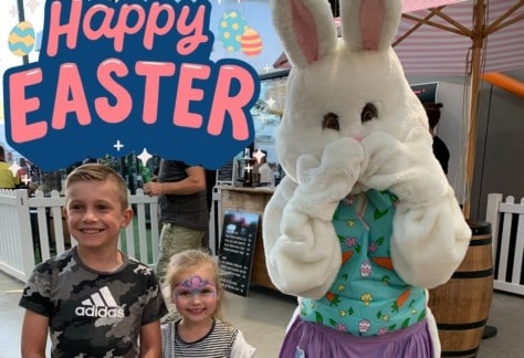 A boy and a girl standing next to Easter Bunny.
