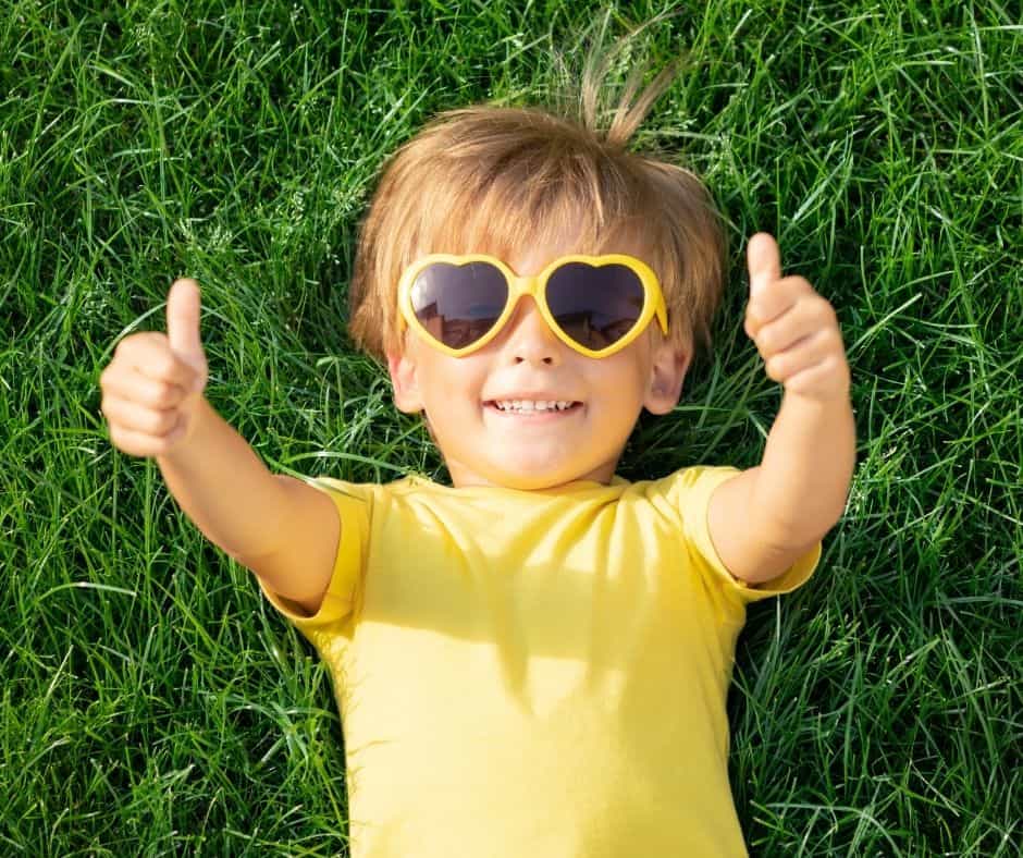 Child looking happy on grass with thumbs up