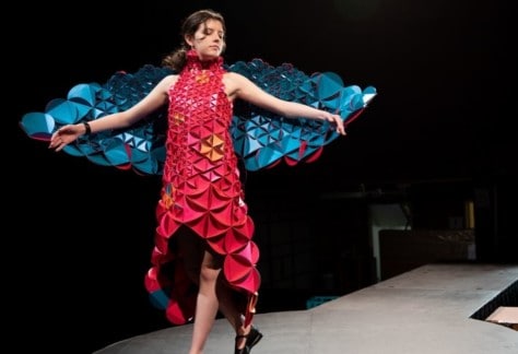 A woman dressed in a red and blue dress made of paper, showcases the wearable art work on the cat walk.