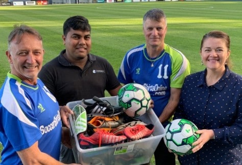 Four people standing next to each other holding soccer gear which is being donated to help seasonal workers play in the social roster.