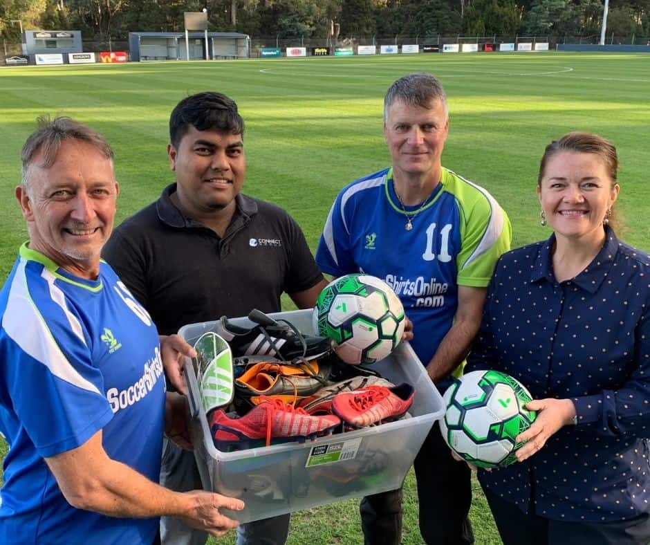 Four people standing next to each other holding soccer gear which is being donated to help seasonal workers play in the social roster.