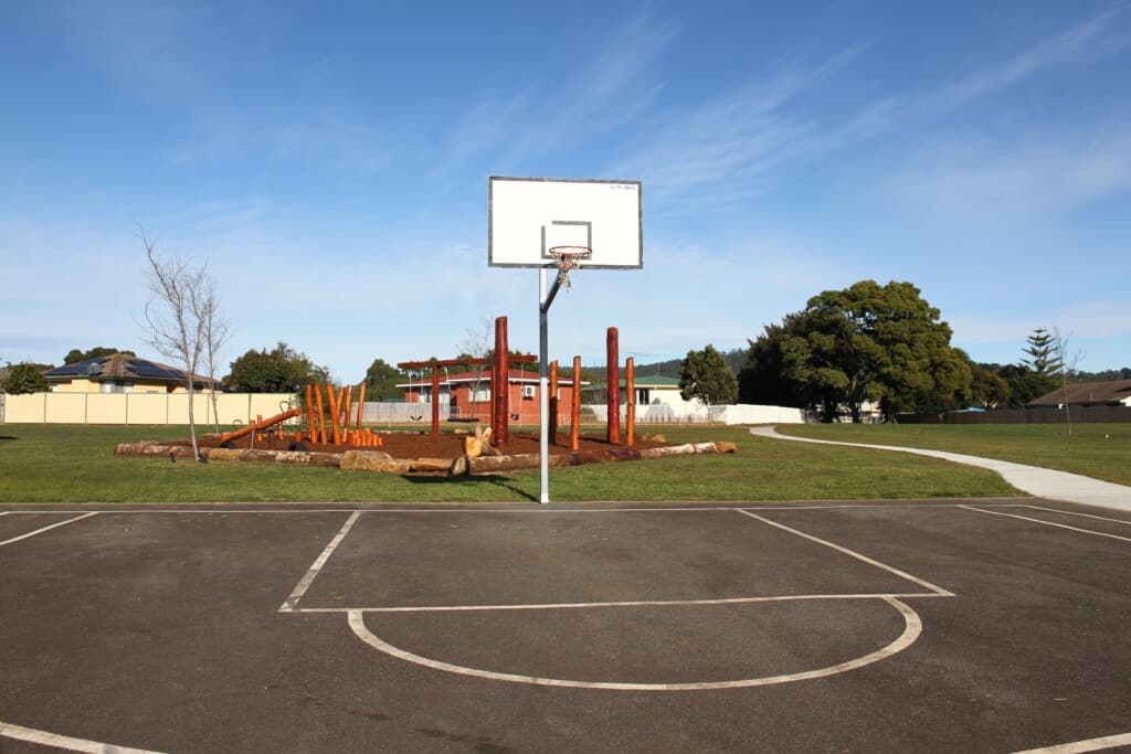 Half a basketball court with a nature playground in the background