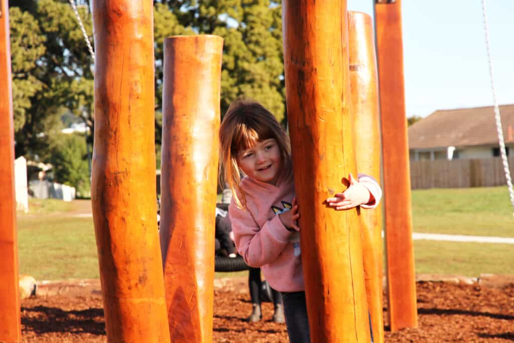 A child peaks out from behind a climbing pole