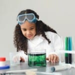 A Child Scientist is cooking up something colourful in a beaker