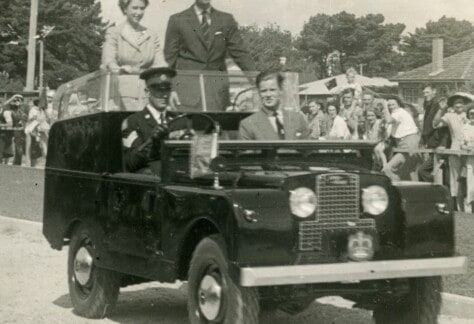 Old photo of Queen Elizabeth II and Prince Philip standing in the back of a car waving to a crowd on onlookers in Devonport in 1954.