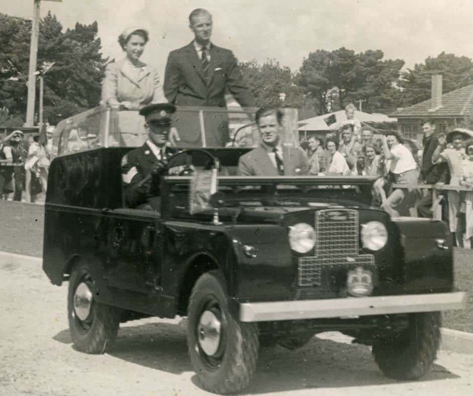 Old photo of Queen Elizabeth II and Prince Philip standing in the back of a car waving to a crowd on onlookers in Devonport in 1954.