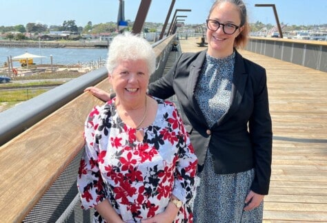 Two women standing next to each other on the elevated walkway in Devonport. The two women are Devonport Mayor Annette Rockliff and Novotel Devonport General Manager Ana Royal overlook the new waterfront park, where the Tasmanian Symphony Orchestra will hold a free concert called Symphony on the Waterfront next year.