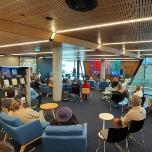 A group of people sit in the Library watching a performance