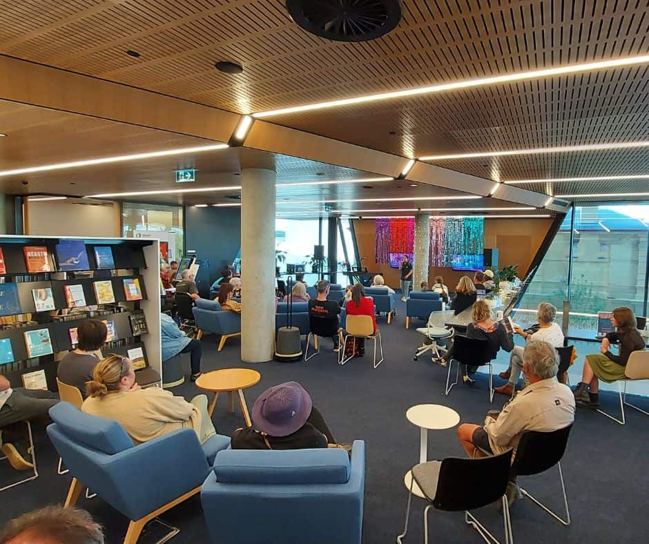 A group of people sit in the Library watching a performance
