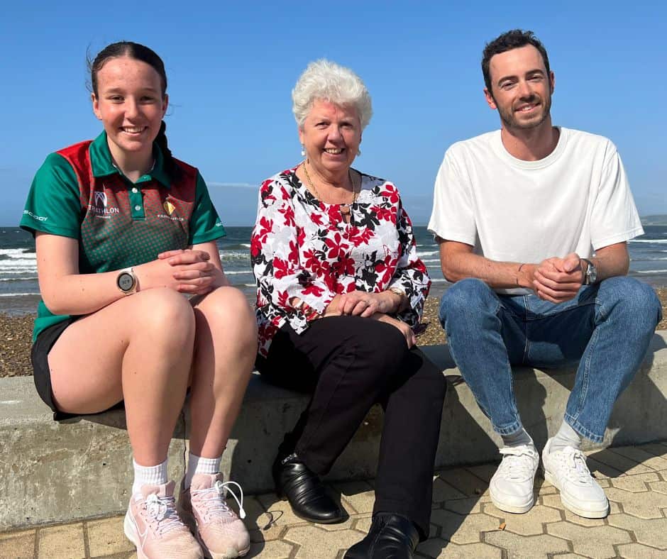 Three people sitting next to each other with the beach in the background. Devonport Mayor Annette Rockliff (centre) with Devonport junior triathlete Erina McLachlan and Olympian triathlete Jake Birtwhistle (Launceston) at a recent announcement that the World Triathlon Para Series is coming to Devonport in 2023, as part of a triathlon Festival next March.