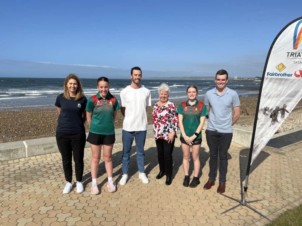 Six people standing in a row infront of the beach. At a recent announcement that the World Triathlon Para Series is coming to Devonport in 2023, as part of a triathlon Festival next March, are (from left) Triathlon Tasmania State Service Manager Shellie Casalegno, Devonport junior triathlete Erina McLachlan, Olympian triathlete Jake Birtwhistle (of Launceston), Devonport Mayor Annette Rockliff, Launceston junior triathlete Matilda Bosworth and Tri Events Tasmania Managing Director Will Blackaby.