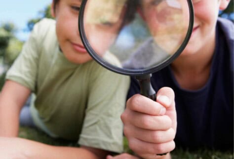 Two children looking through a magnifying glass whilst lieing on grass
